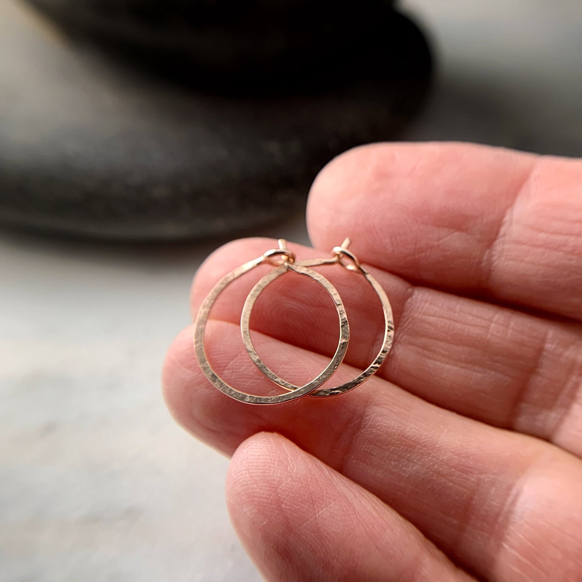 two rose gold hammered hoop earrings shown on a hand for scale