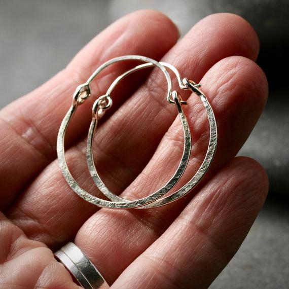 hammered sterling silver hoop earrings with a latching ear wire shown on a hand for scale