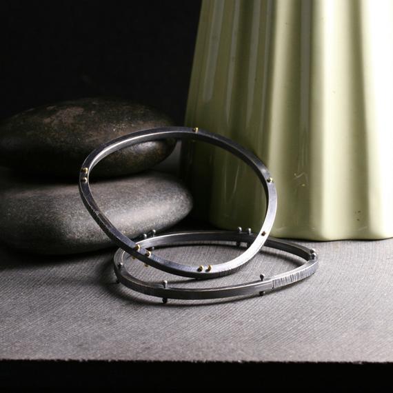 two bracelets shown from above to show the asymmetrical shape and the rivets