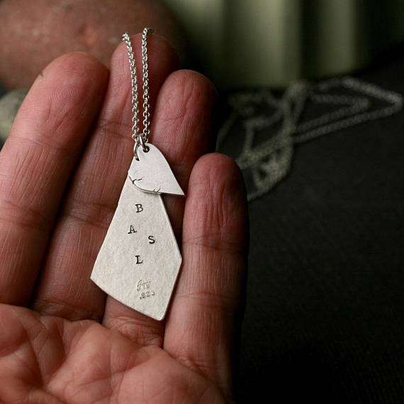 triangular shaped silver pendant with stamped initials and a chunky heart.  shown on a hand for scale