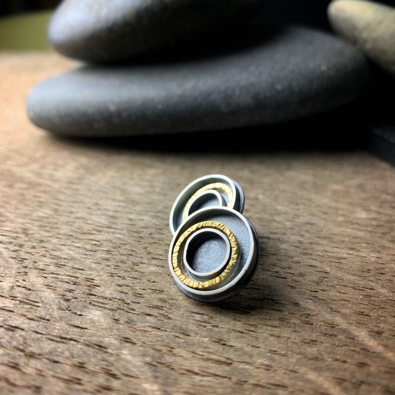 oxidized silver earrings with concentric circles, one of which is yellow gold