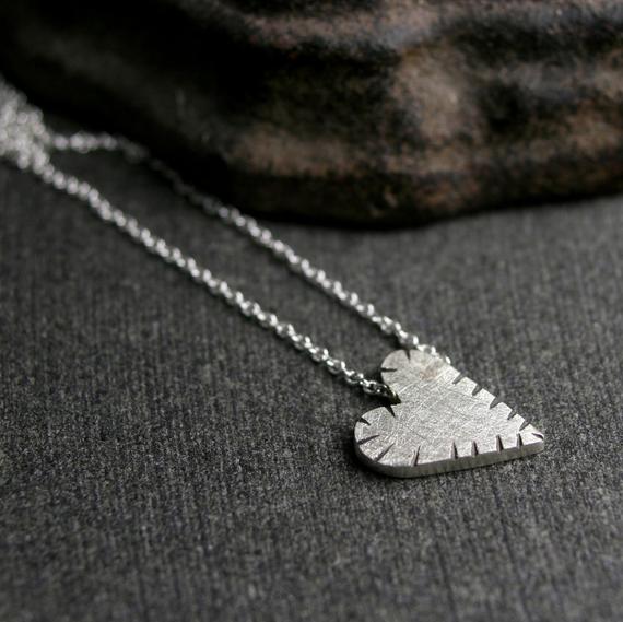 A sterling silver tiny cut heart pendant with a chain, displayed on a dark background.