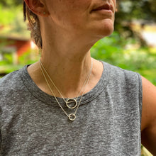 Load image into Gallery viewer, two pendants, one large and one small, in sterling silver.  They are circles with a hammered texture and the chain runs through the circle.  Shown on a model for scale
