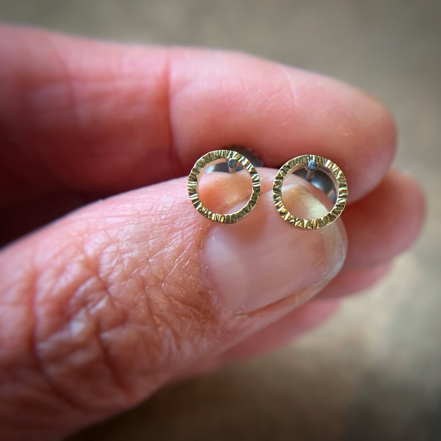 quarter inch yellow gold circles with hammered texture and oxidized silver posts and backs.  Shown being held in a hand for scale