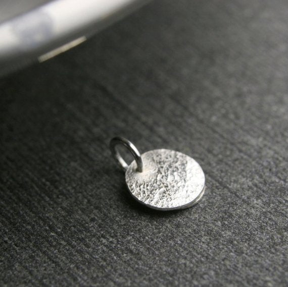 tiny disc with hammered texture showing the back of the pendant