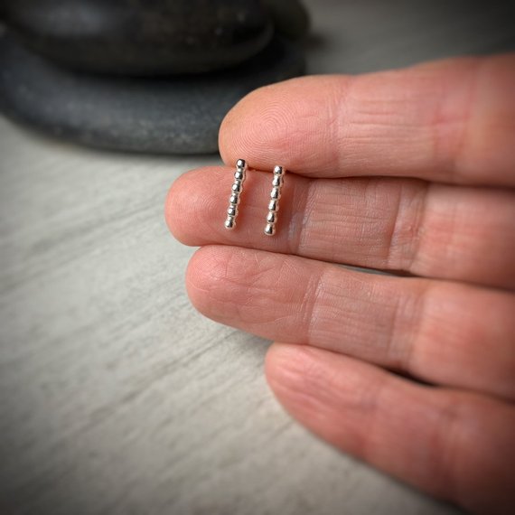 Tiny sterling silver beaded bar stud earrings, front view on a hand for scale