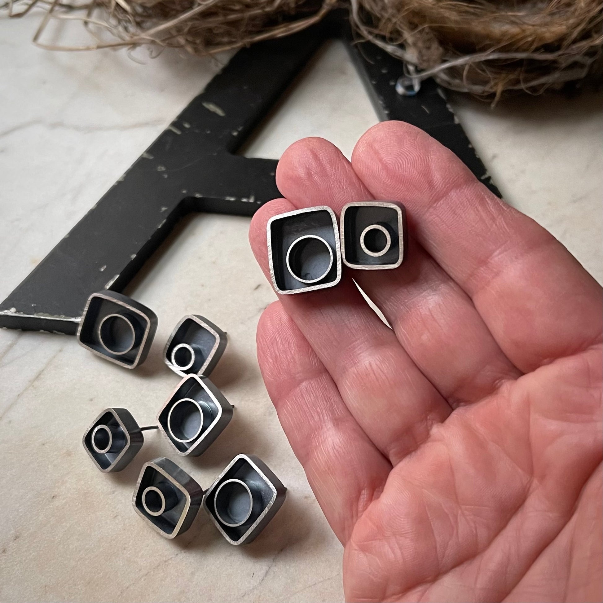 All eight earrings with a large earring and a small earring held in a hand for scale