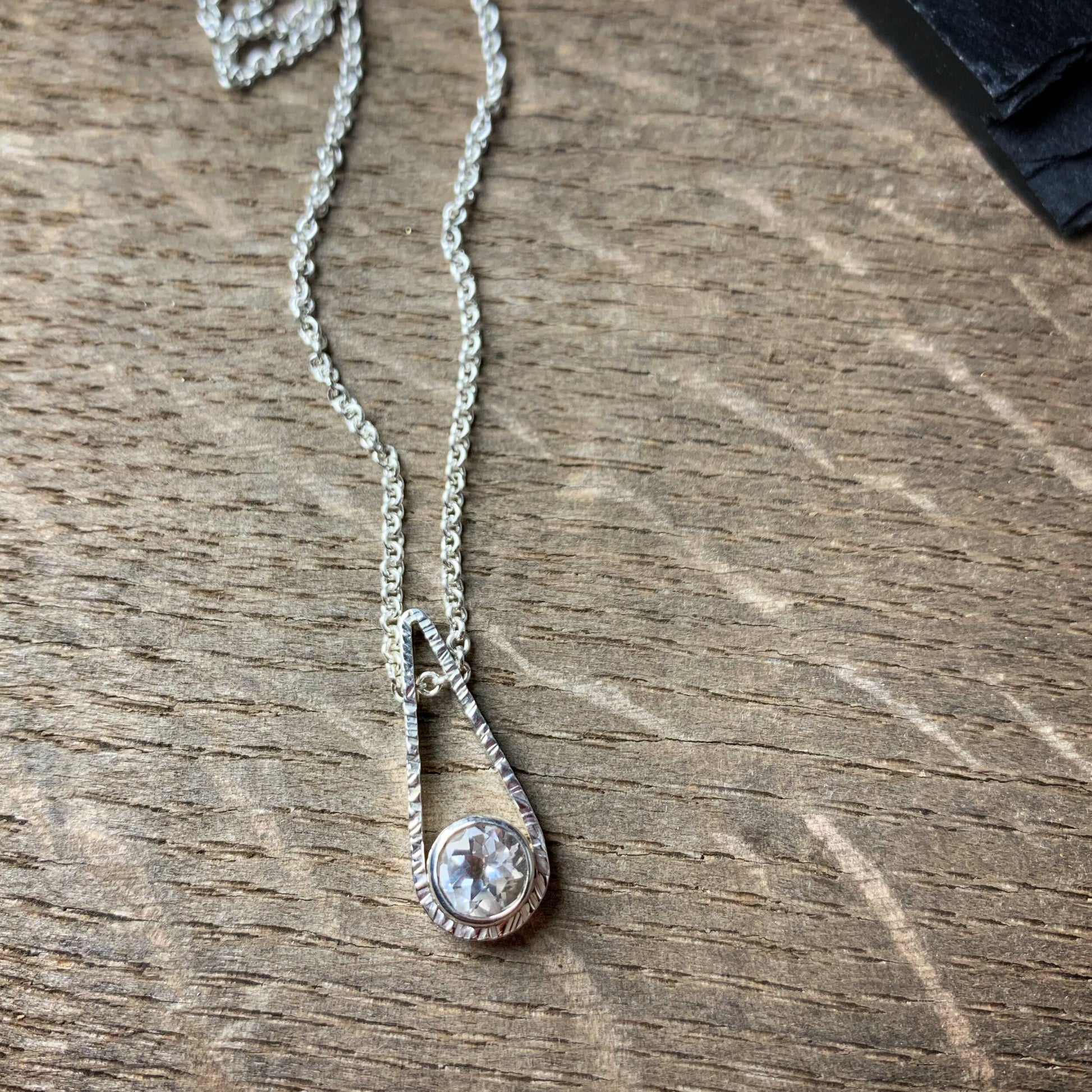a round 6mm bezel set white topaz in a teardrop shaped textured pendant