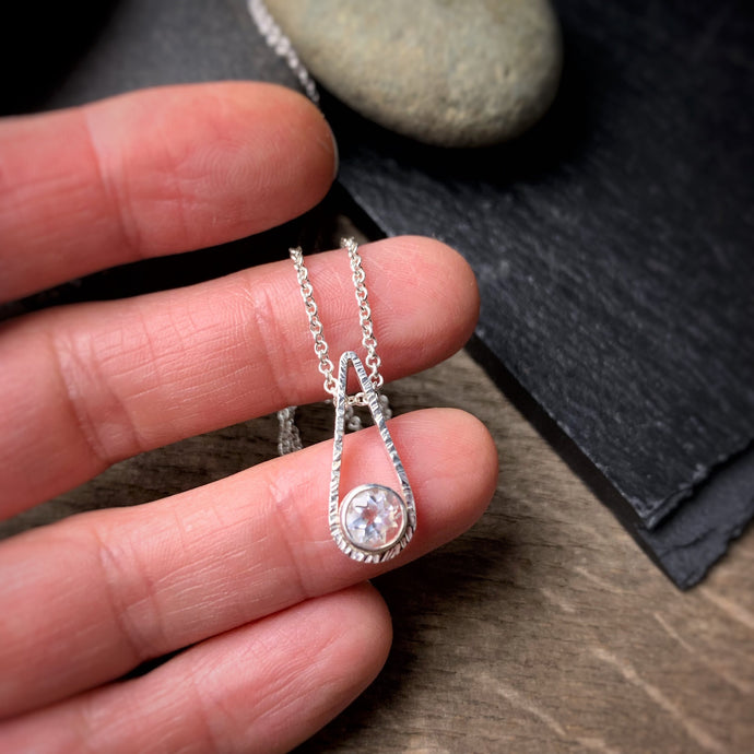 a 6mm white topaz set in a bezel and set into the bottom of a teardrop shaped textured pendant