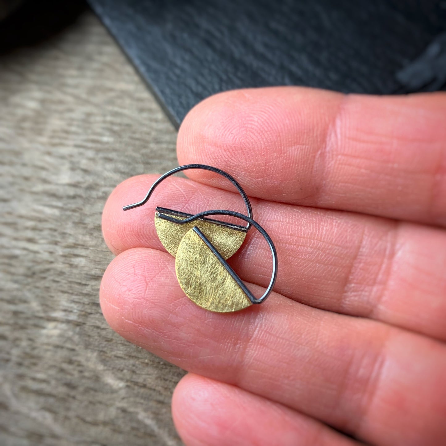 hoop earrings with half discs of 18k yellow gold with oxidized ear wires hoop shown on a hand for scale